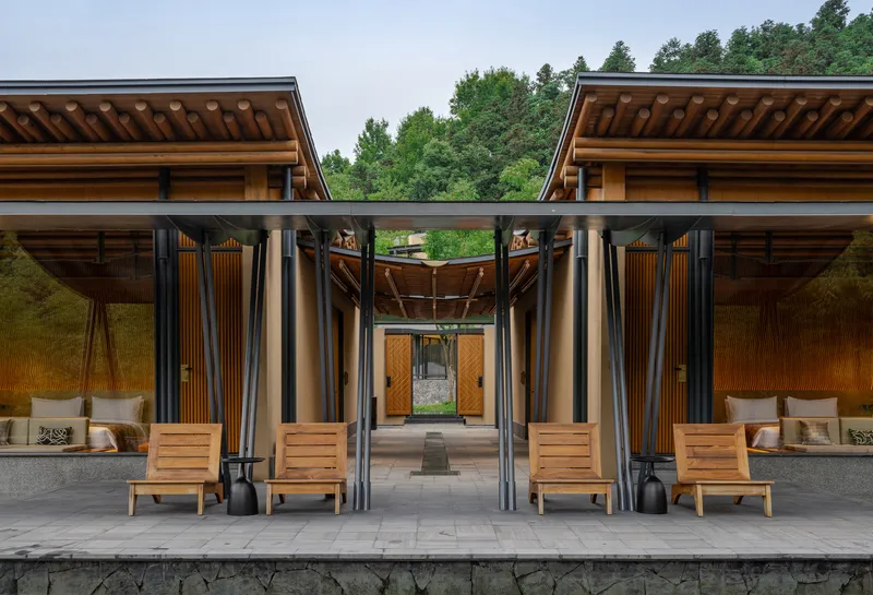 Covered terrace with timber roof, steel columns, and wooden lounge chairs facing a forested hillside