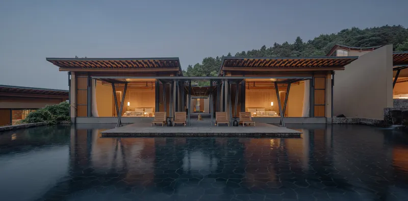 Twin pavilions with exposed timber roofs flanking a reflecting pool at dusk