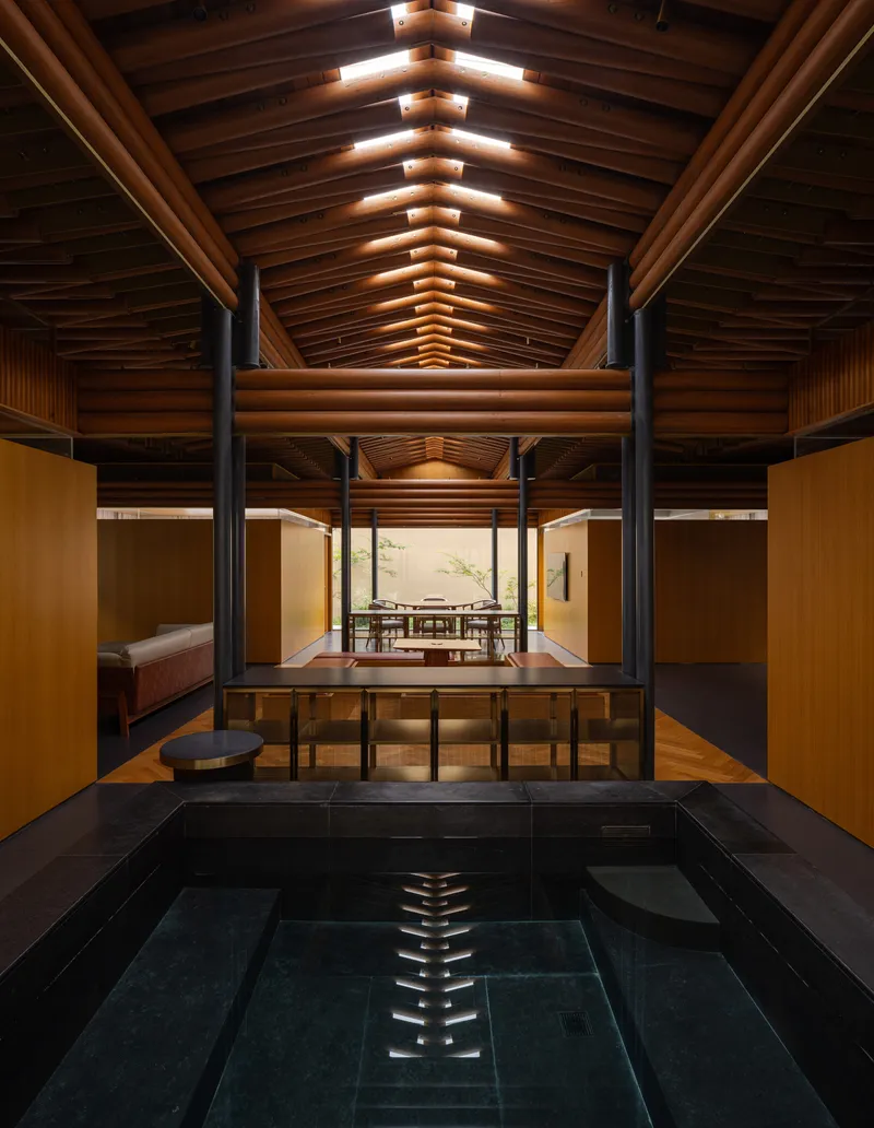 Indoor bath with dark tile surround beneath a vaulted timber ceiling with steel bracing