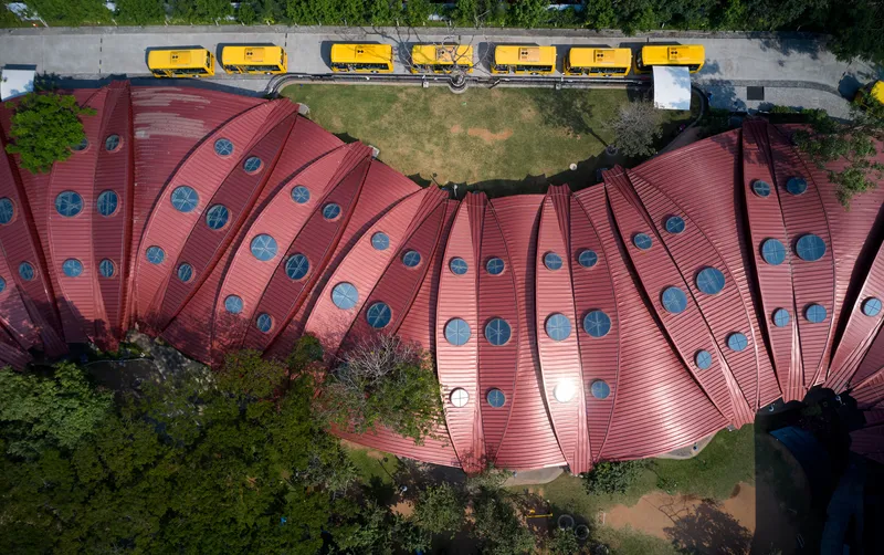Drone view of the fanned metal roof with circular skylights beside a row of yellow buses