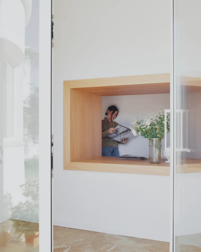 Timber-lined window nook with a person reading while standing beside a vase of flowers