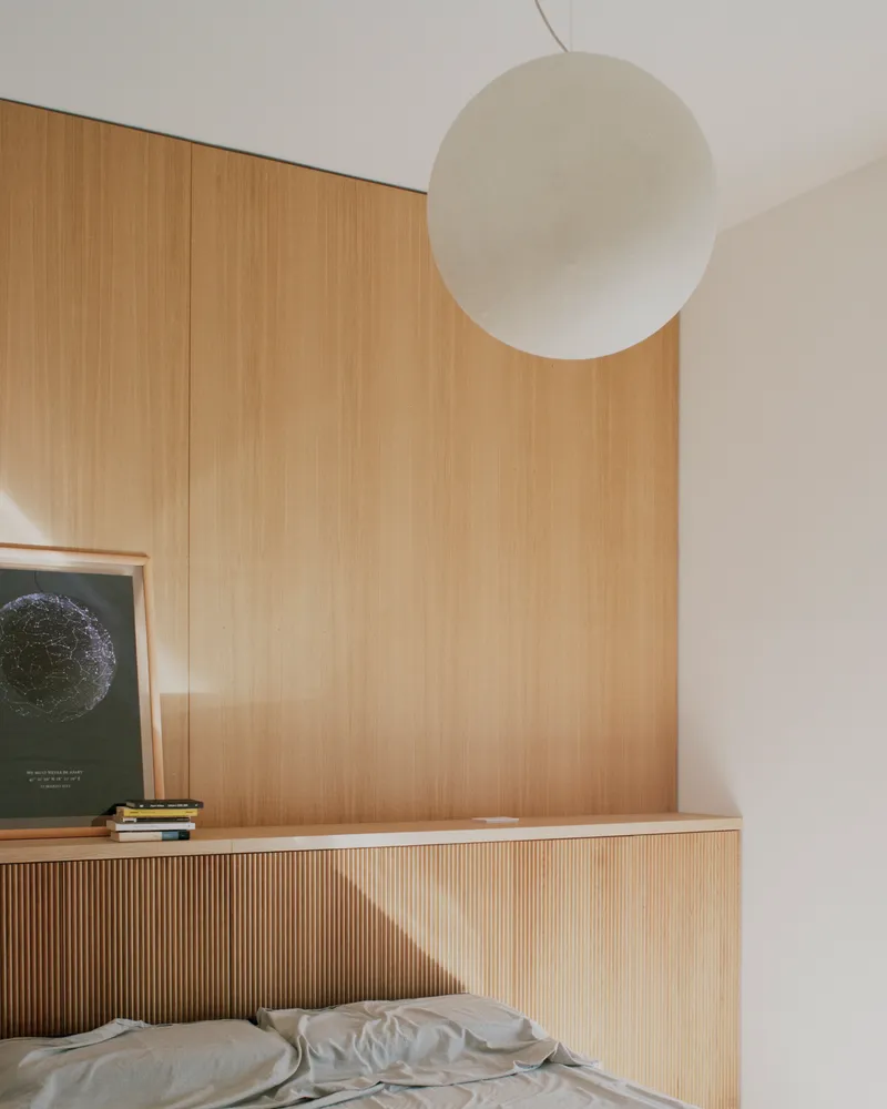 Bedroom corner with ribbed oak headboard wall and spherical pendant light above the bed