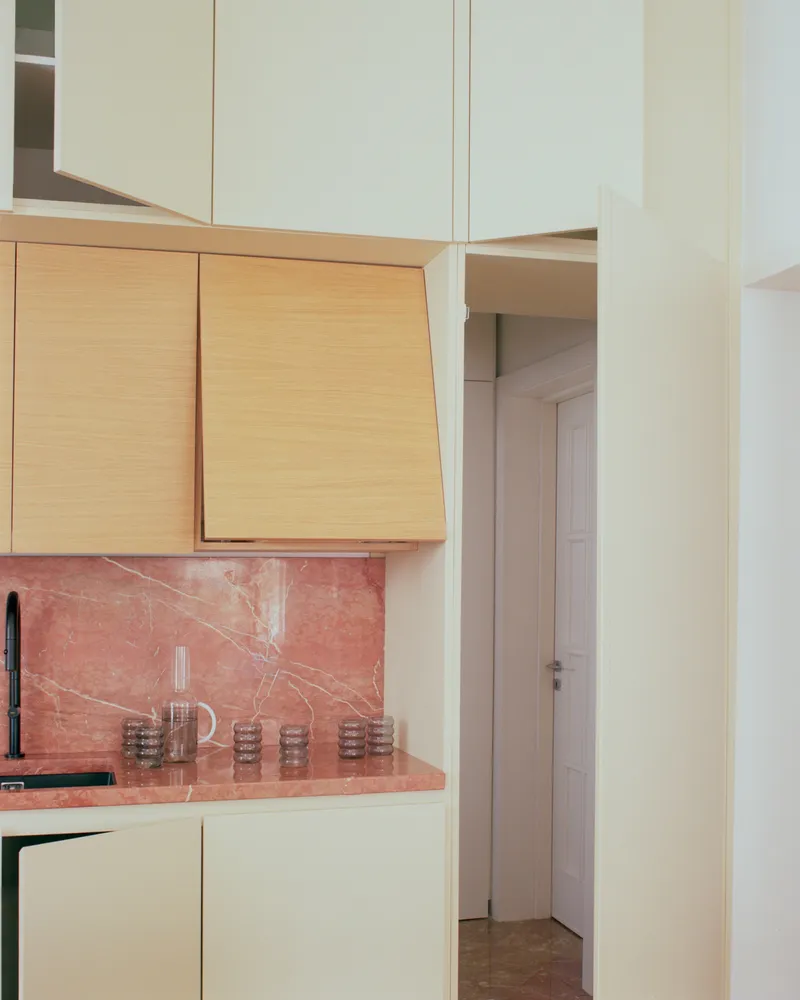 Kitchen corner showing oak cabinetry above pink marble backsplash with glass tumblers on the counter