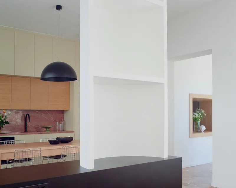 Open plan interior with kitchen visible beyond a dark island and recessed wall niche framing vases
