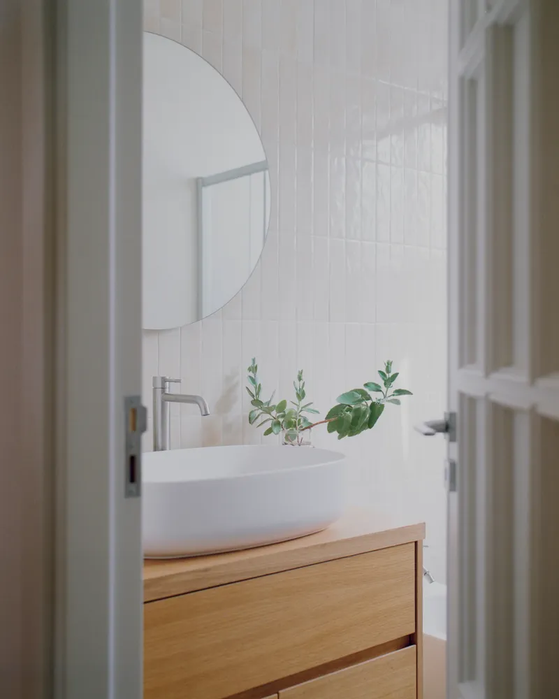 Bathroom vanity with vessel sink on oak cabinetry beneath vertical white tiles and a round mirror