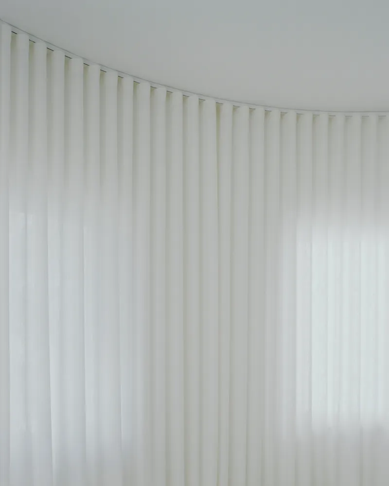 Close-up of translucent white ribbed curtain curving along a ceiling track in soft daylight