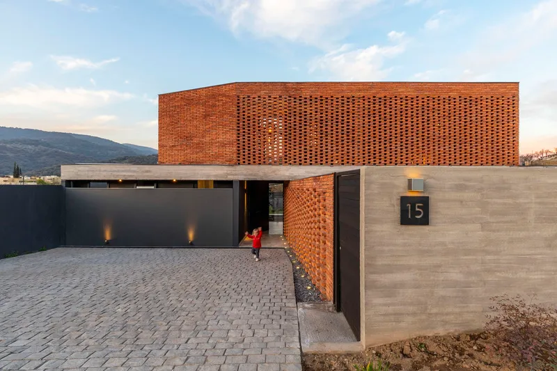 Entry courtyard with perforated brick volume above concrete base and child in red crossing the paving