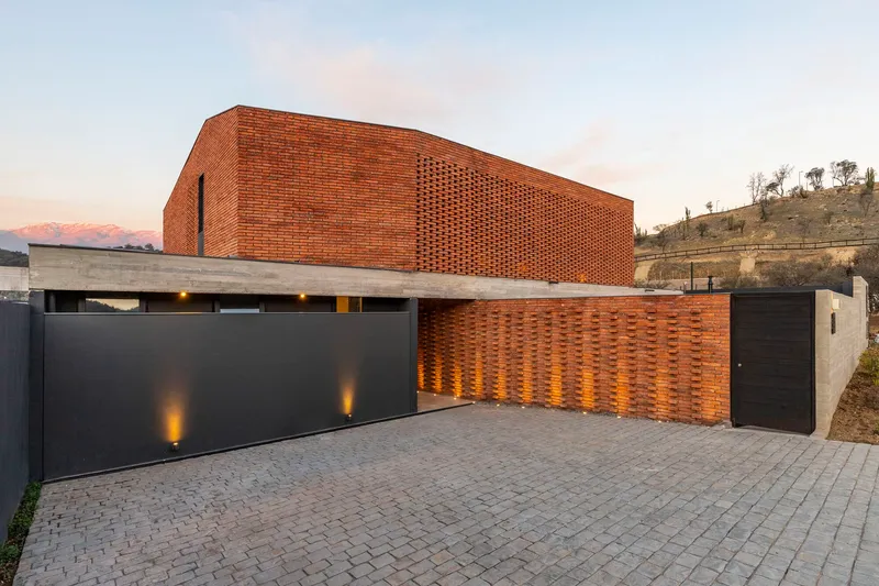 Street facade showing perforated brick upper level cantilevered over dark metal gates at dusk