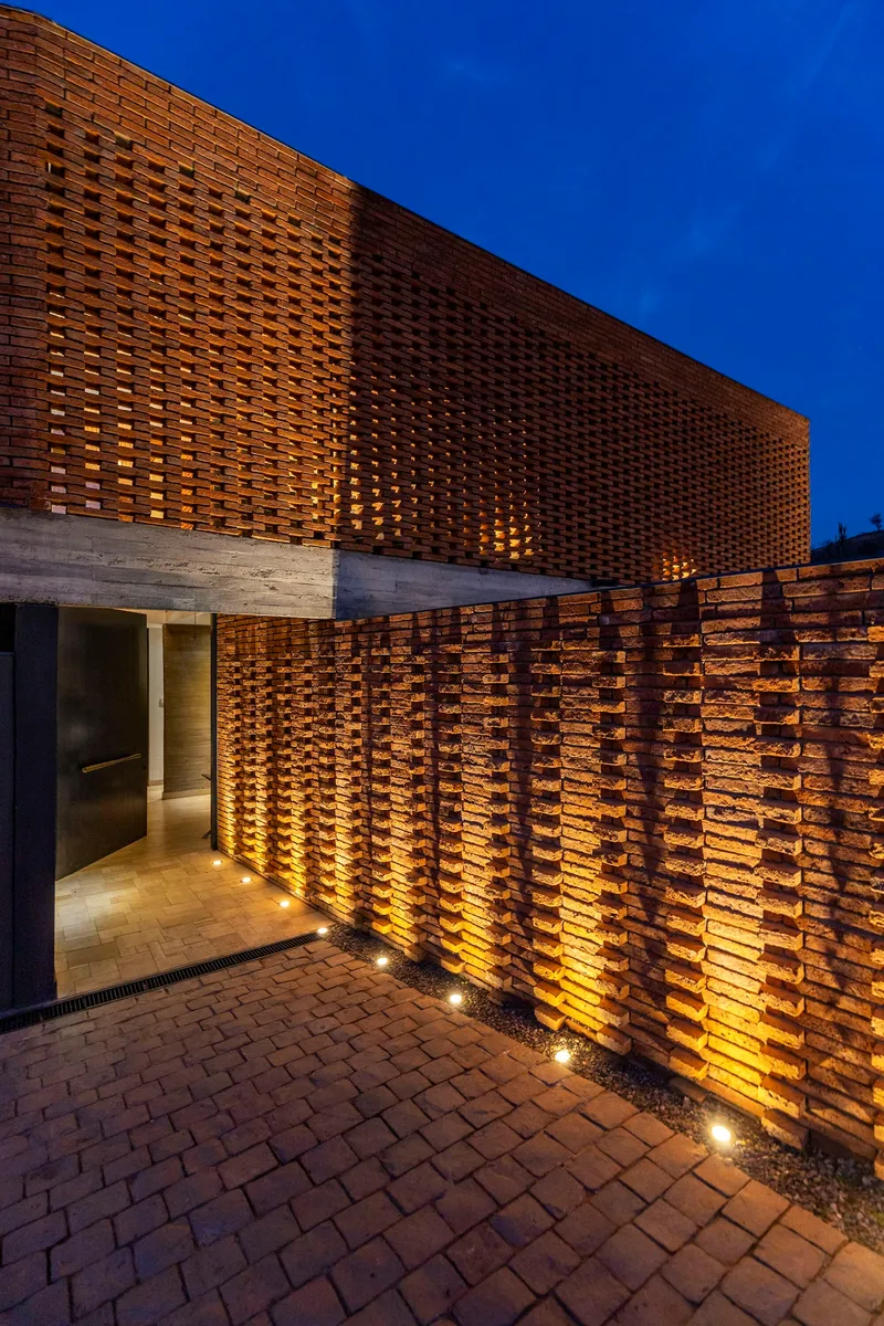 Perforated brick screen wall with uplight grazing the textured surface at blue hour