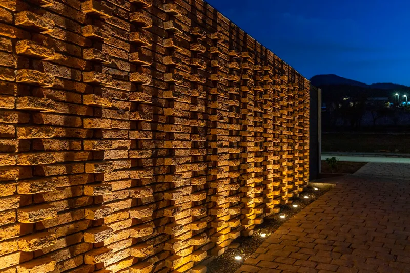 Close-up of staggered brick wall with ground-level uplighting illuminating the relief pattern at dusk