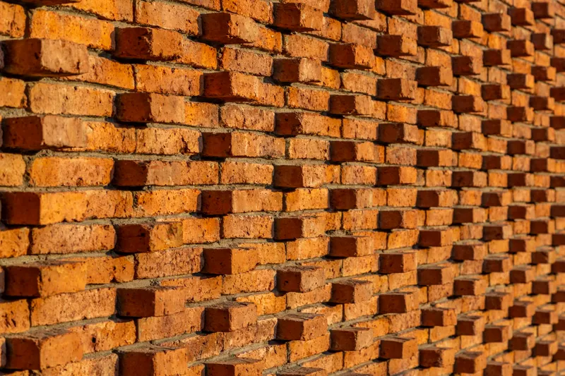 Close-up of perforated brick screen wall with alternating protruding bricks casting diagonal shadows in afternoon light