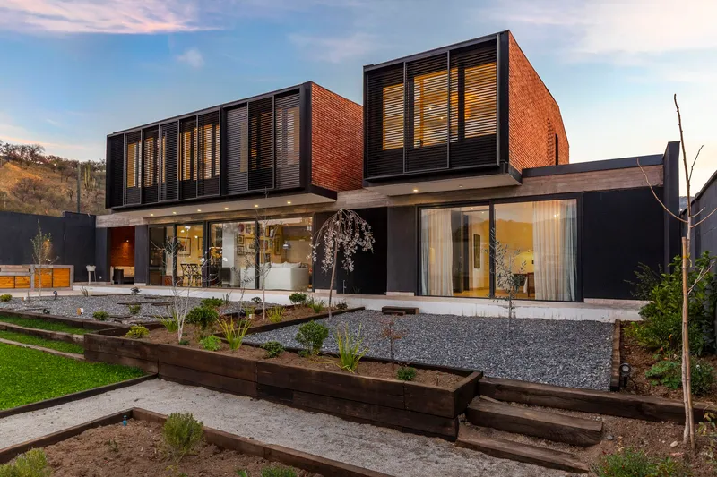 Garden view showing the elevated red brick volumes with horizontal louvers above terraced planted beds and gravel courtyard