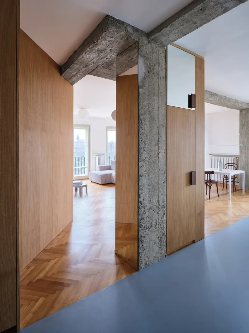 Oak-clad partition alongside exposed concrete column framing view into living area with herringbone parquet