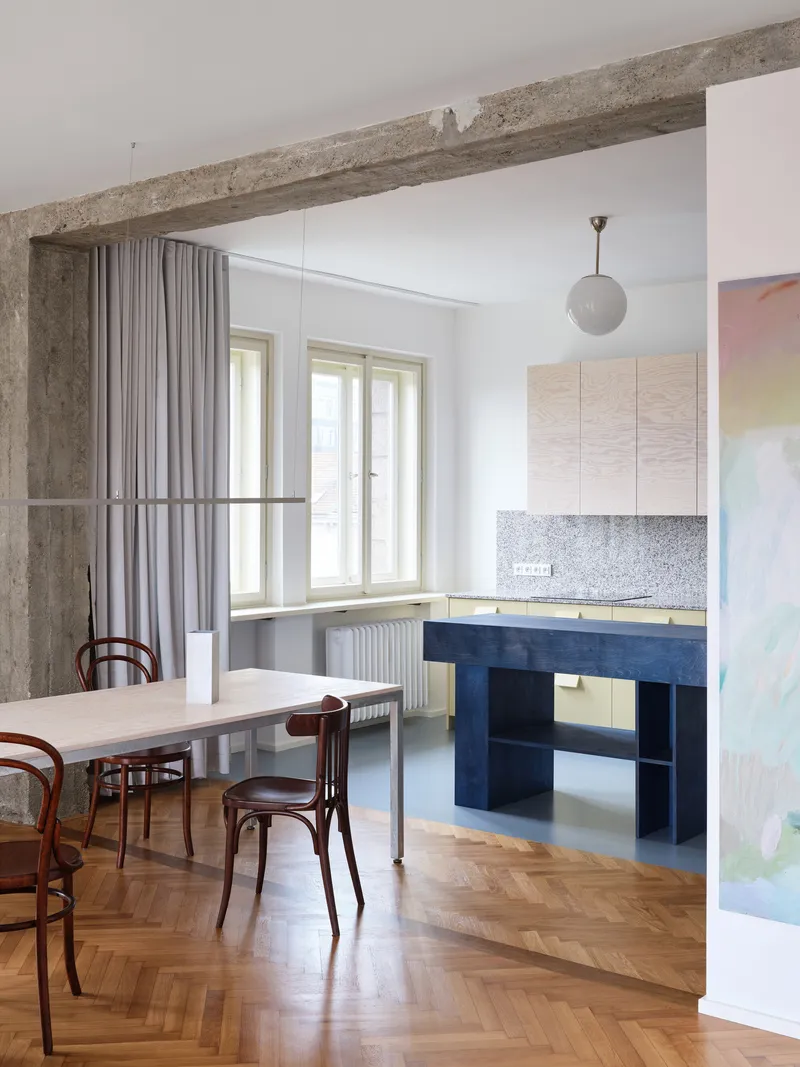 Kitchen area with blue island, terrazzo backsplash and fabric curtain room divider under concrete beam
