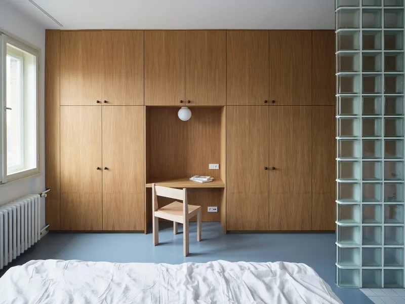 Bedroom with oak wardrobe wall, integrated desk nook and glass block partition beside the bed