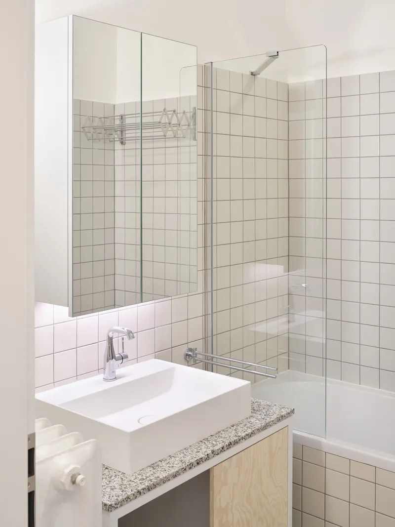 White basin on terrazzo counter with plywood cabinet and glass block partition visible at right