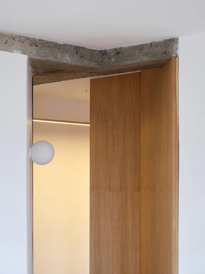 Doorway detail showing exposed concrete lintel above timber door frame with globe light visible beyond