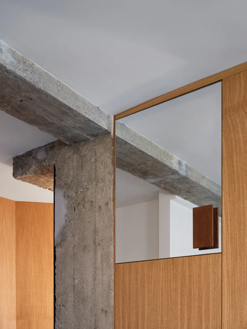 Detail of exposed concrete beam meeting oak-framed glazed partition above wood cabinetry