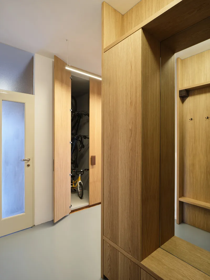 Entry hallway with oak storage wall revealing bicycle closet with linear LED lighting