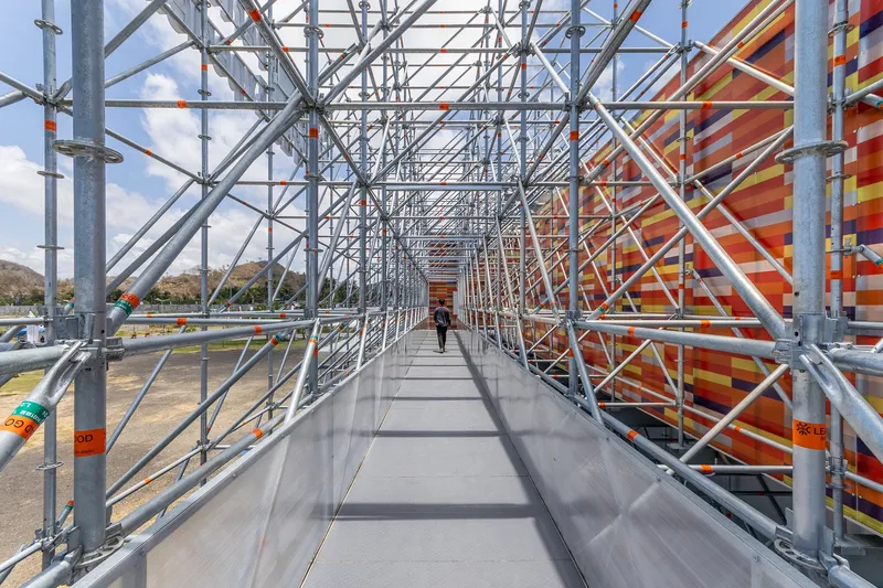 Elevated walkway through the steel scaffolding structure with a figure walking toward the horizon