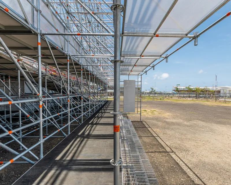Covered walkway with steel scaffolding columns and translucent canopy panels under midday sun