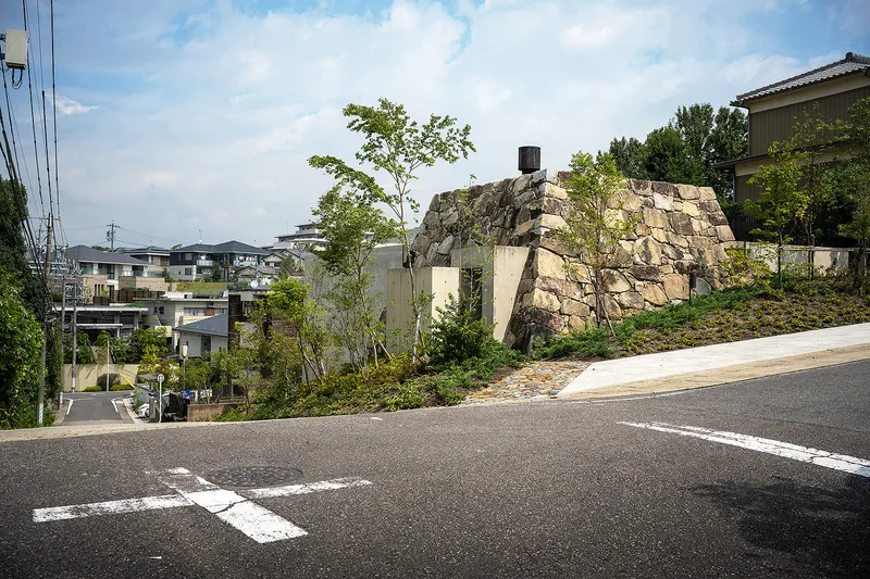 Street view of the boulder-like stone structure atop a graded hillside with young trees