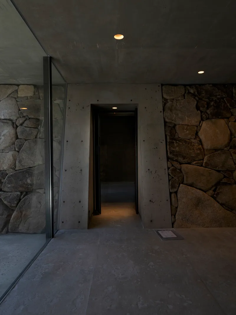Entry corridor framed by rough stone walls and board-formed concrete under recessed ceiling lights