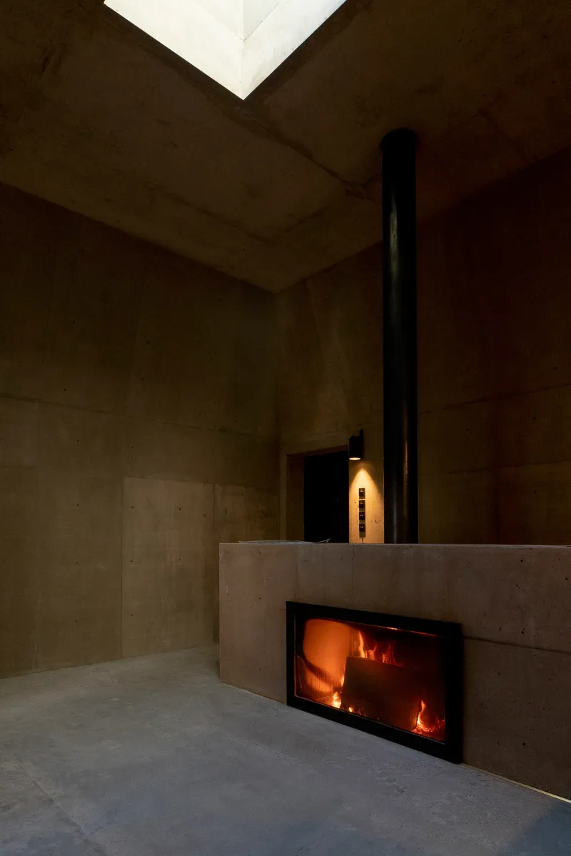 Glass-fronted fireplace set into a concrete volume beneath a black metal flue and skylight