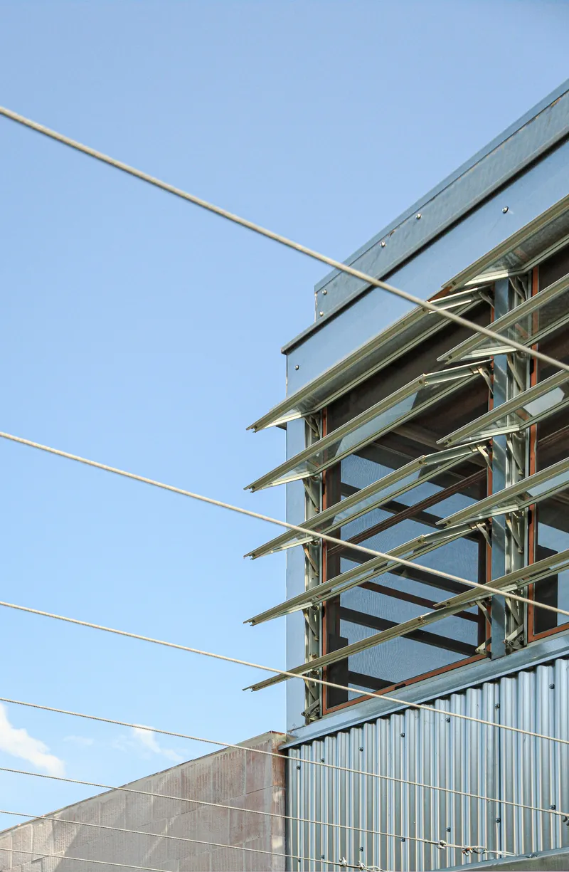Exposed steel frame structure with horizontal beams crossing diagonal tension cables against a clear sky