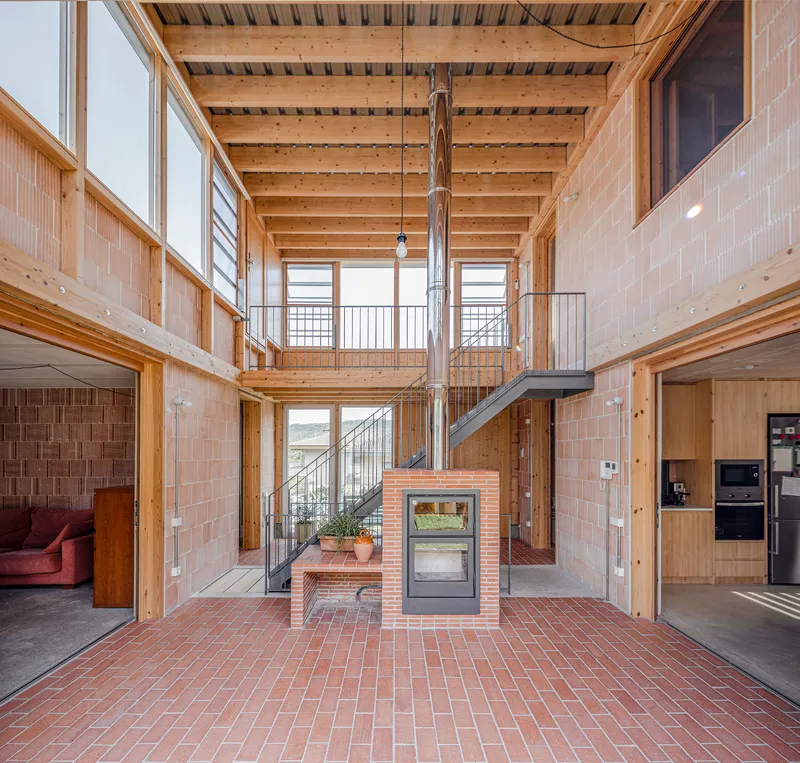 Central atrium with timber ceiling structure, steel staircase, and freestanding brick fireplace on herringbone pavers