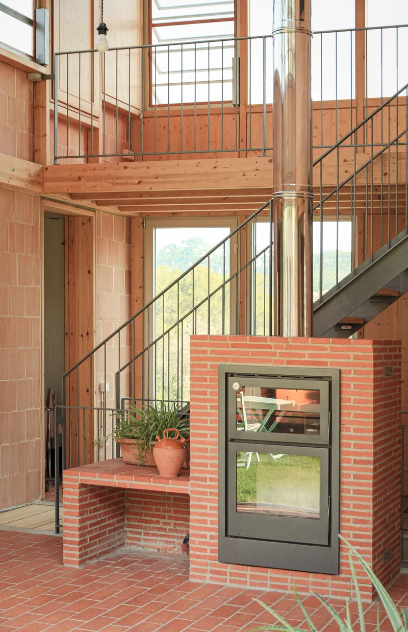 Double-height interior with timber structure, metal stairs, and red brick fireplace beside a potted plant
