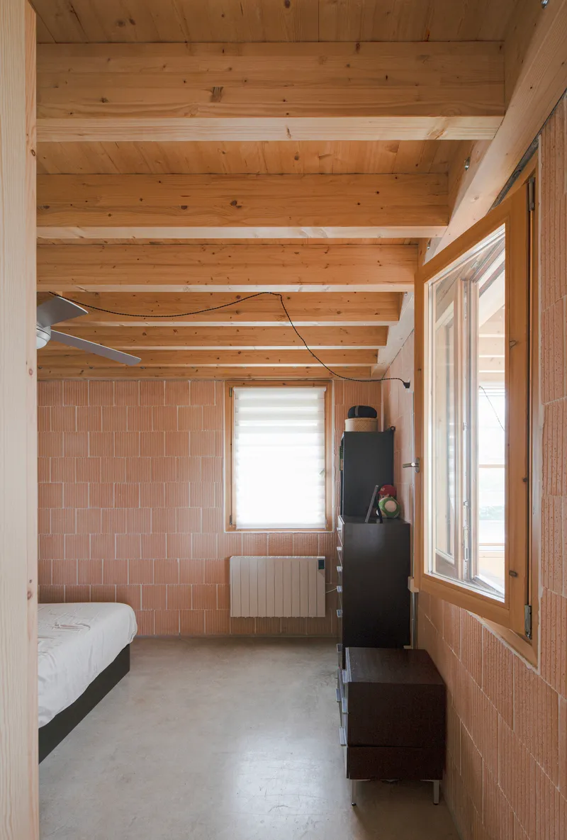 Bedroom with exposed timber beams, terracotta tile wall panels, and polished concrete floor