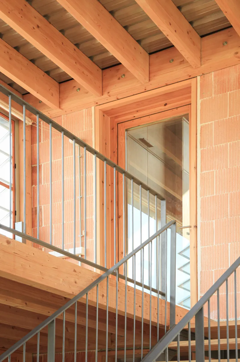 Stairwell detail with metal railing, timber ceiling joists, and terracotta block wall under natural light