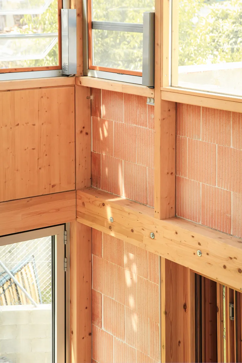 Detail of timber framing intersecting with vertical terracotta tile infill panels at a window corner