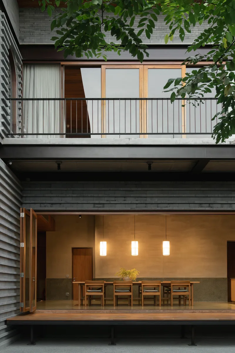 Dining room opening to courtyard through sliding doors at dusk with pendant lights illuminated