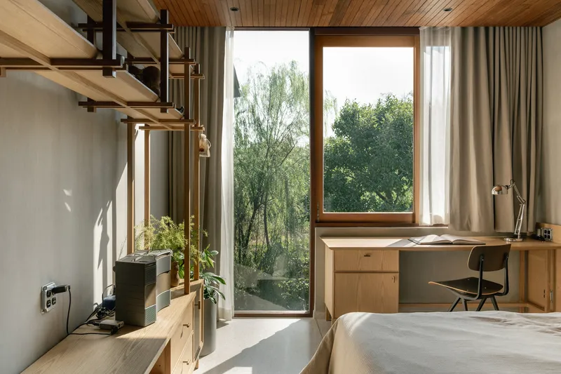 Bedroom with timber-lined ceiling, corner windows framing trees, and a built-in desk receiving morning light