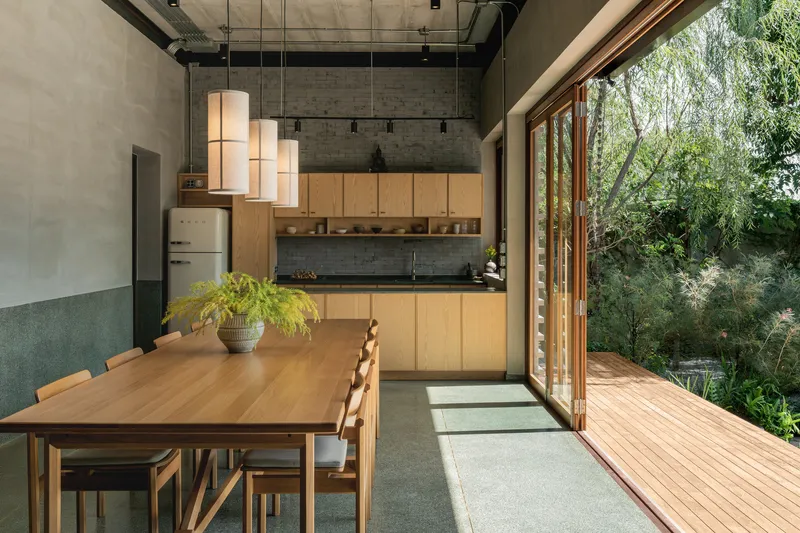 Kitchen and dining space opening onto a timber deck through floor-to-ceiling glazed doors with garden beyond