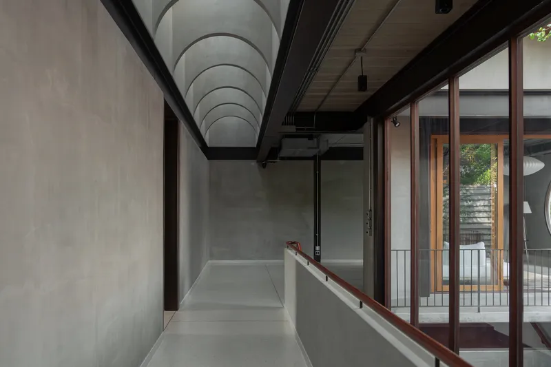 Upper corridor with vaulted concrete ceiling and timber-framed glazing overlooking an internal courtyard