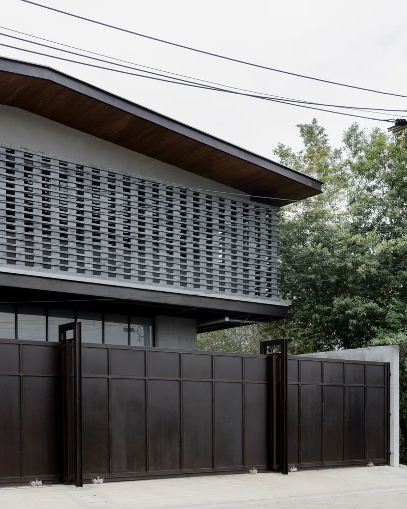 Detail of the woven brick screen wall above the metal gate with trees in the background