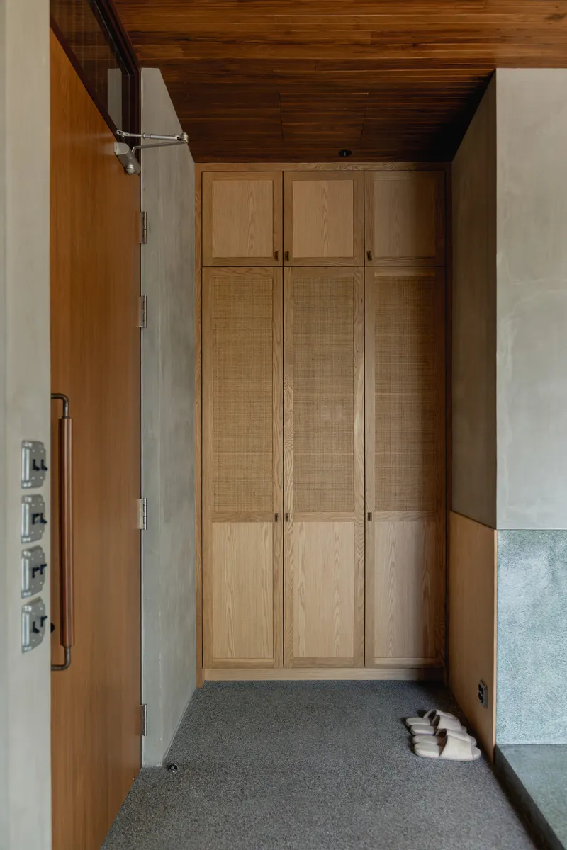Hallway with timber wardrobes featuring woven cane panels beneath a dark wood ceiling