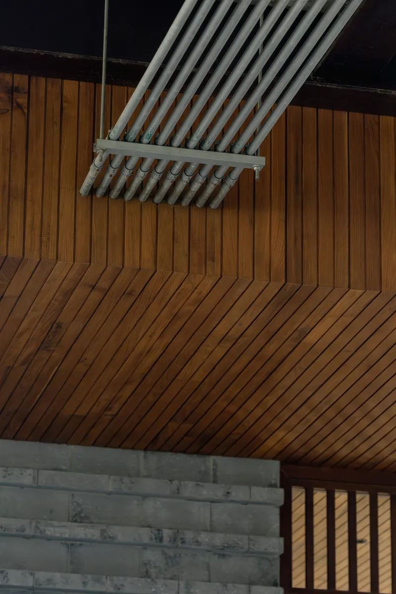 Interior ceiling with diagonal timber slat paneling meeting a skylight frame and concrete block wall