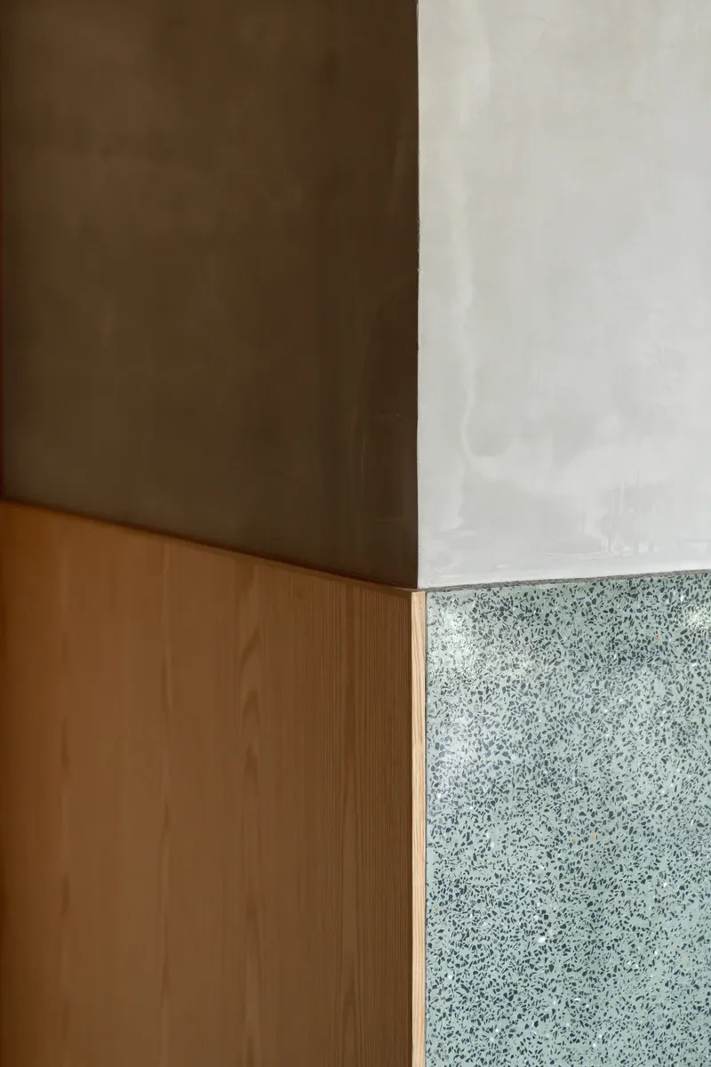 Corner detail where timber cabinetry meets polished concrete ceiling and terrazzo wall panel