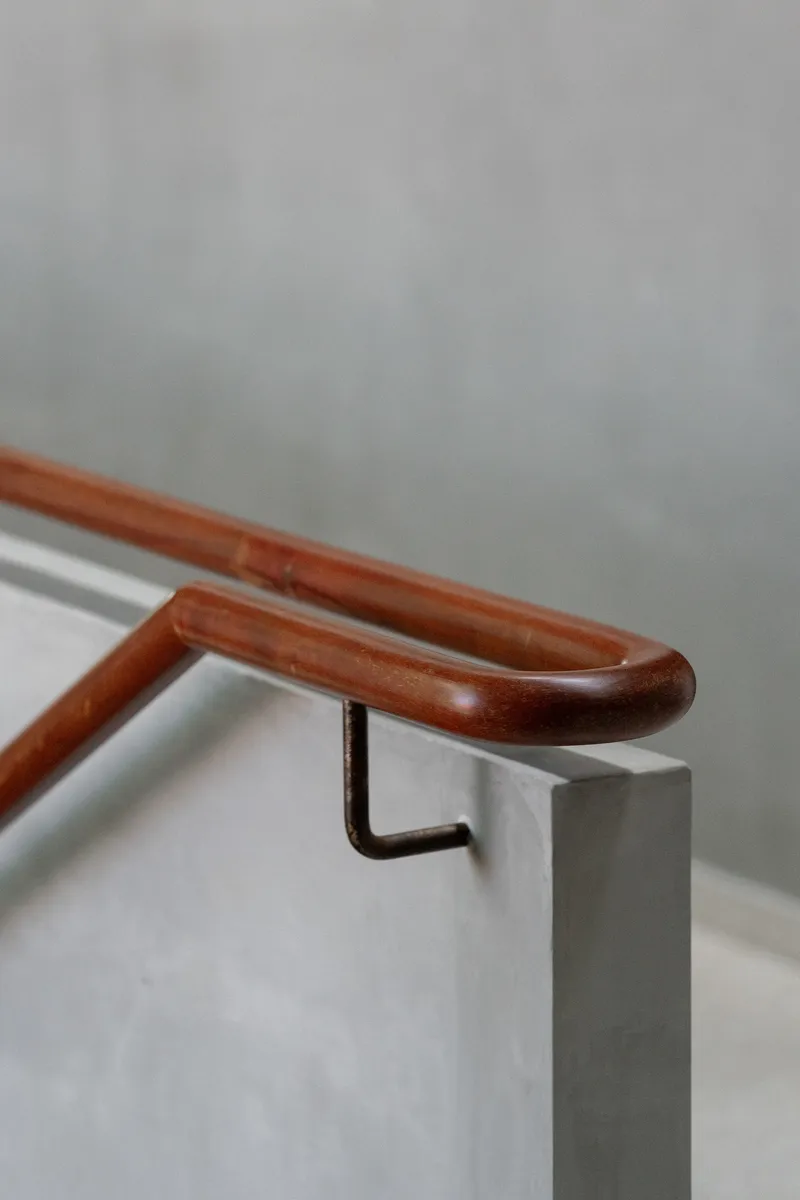 Timber handrail with curved profile secured to concrete wall by black steel bracket