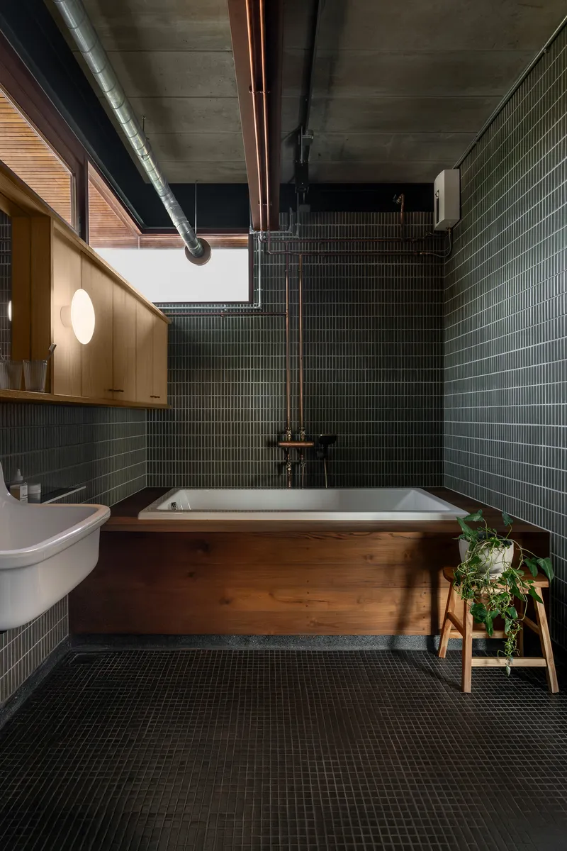 Bathroom with timber-clad tub, dark green subway tiles, and exposed concrete ceiling