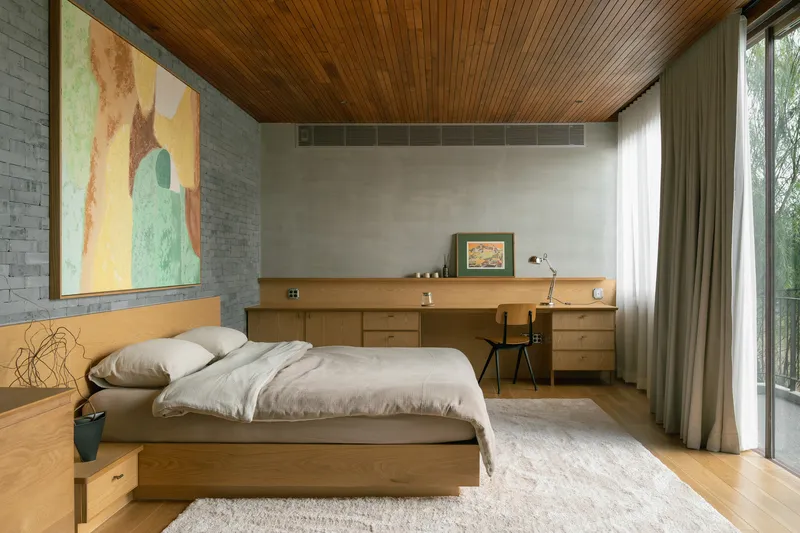 Bedroom with timber slat ceiling, grey brick wall, built-in desk and floor-to-ceiling curtains beside glazed doors