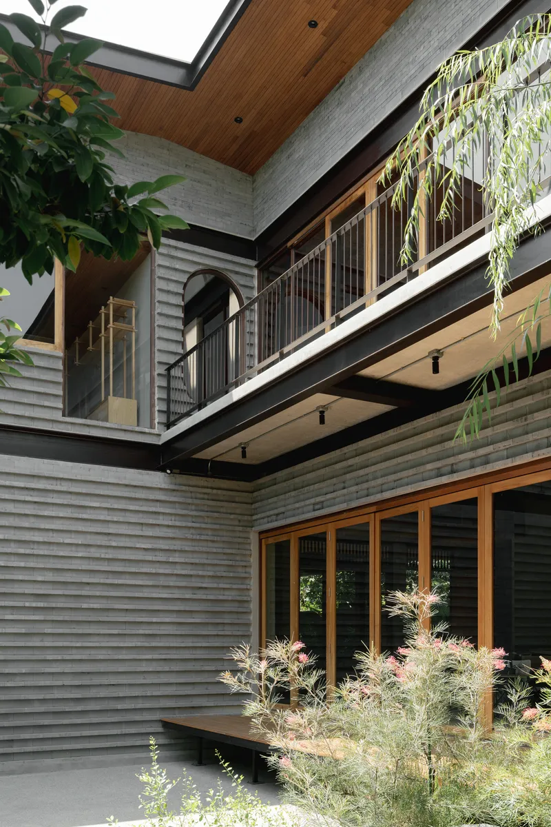 Courtyard view of stacked balconies with timber soffits, horizontal siding and planted beds below overhanging foliage