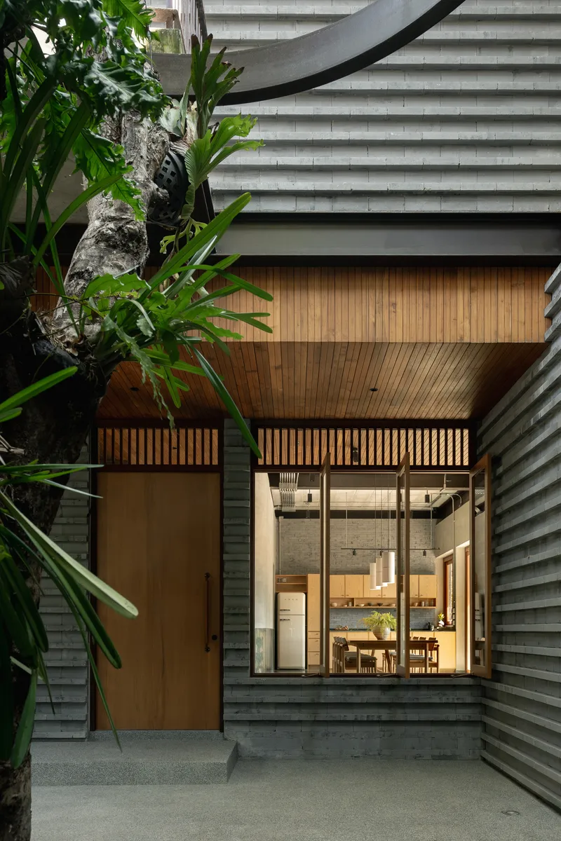 Entry elevation at dusk showing horizontal siding, timber infill panel and glazed opening framing illuminated interior