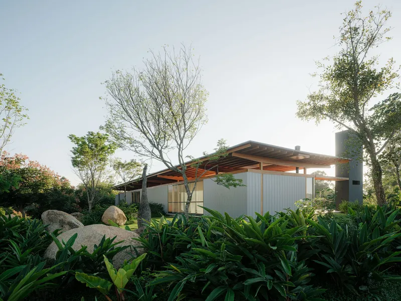 Low-slung timber roof structure with overhangs set among boulders and lush planted beds at dusk