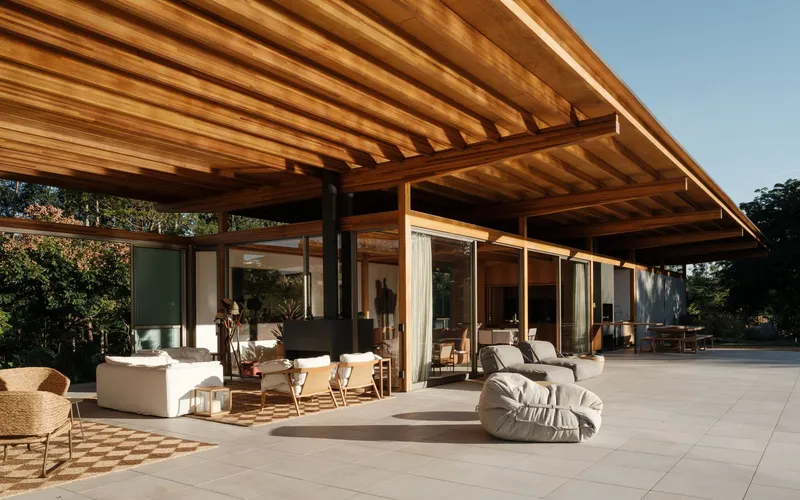 Covered outdoor terrace with exposed timber ceiling beams and floor-to-ceiling glazing framing the interior lounge