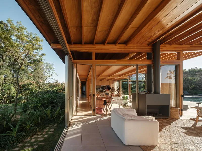 Interior-exterior threshold showing timber ceiling structure with heavy beams and central concrete fireplace core